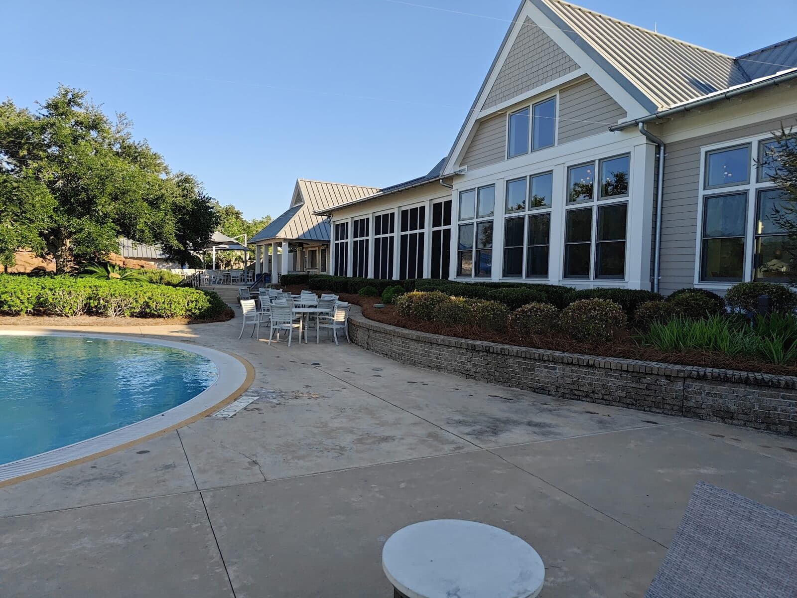 Clubhouse beside a curved pool with fresh pine straw in the raised brick planter and the shrub borders